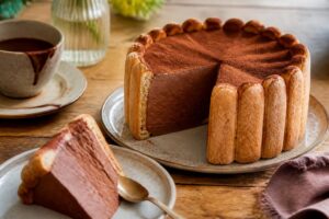 Charlotte au chocolat traditionnelle démoulée sur un plat de service, décorée de copeaux de chocolat et de quelques framboises fraîches